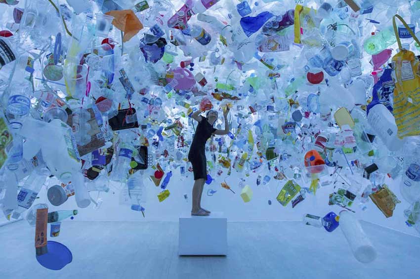 artist surrounded by plastic waste turned into art installation